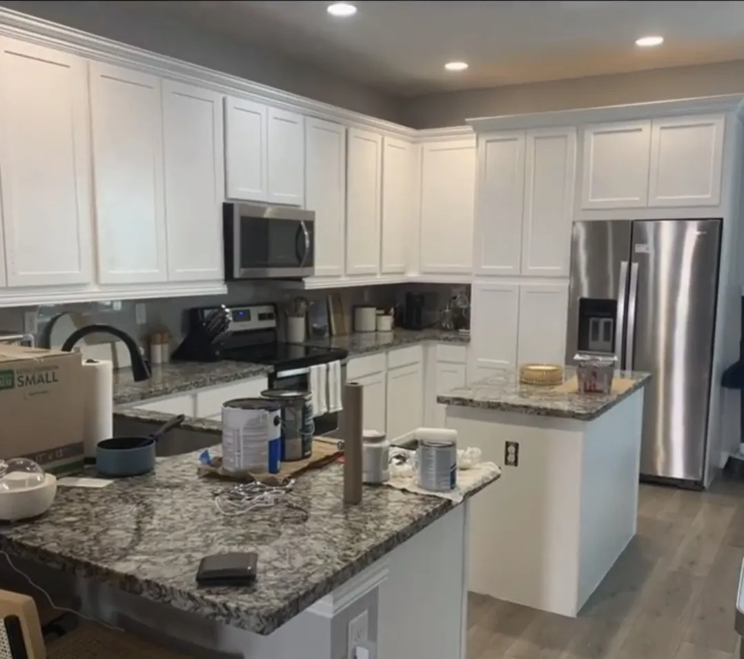 Kitchen cabinets nearly finished in white — paint supplies on counter
