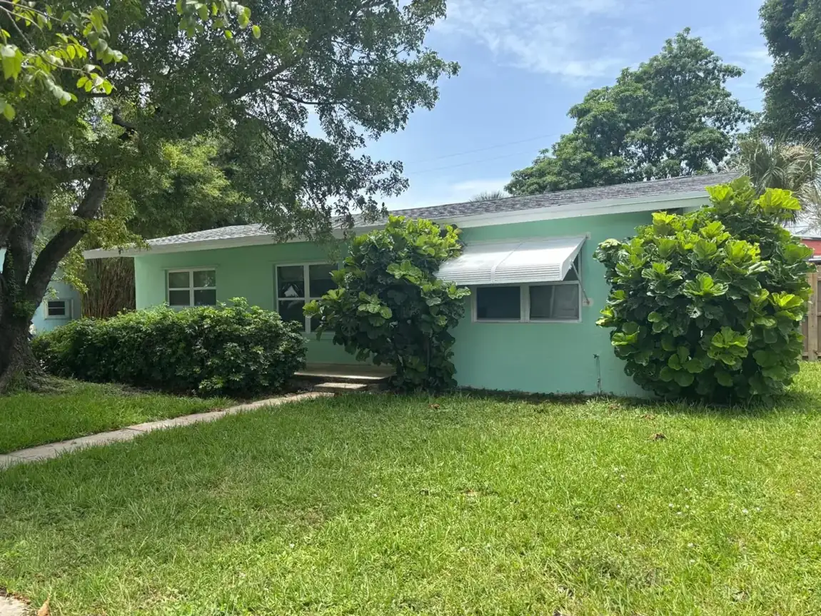 Single-story South Florida ranch house painted mint green, with a white aluminum awning over one window