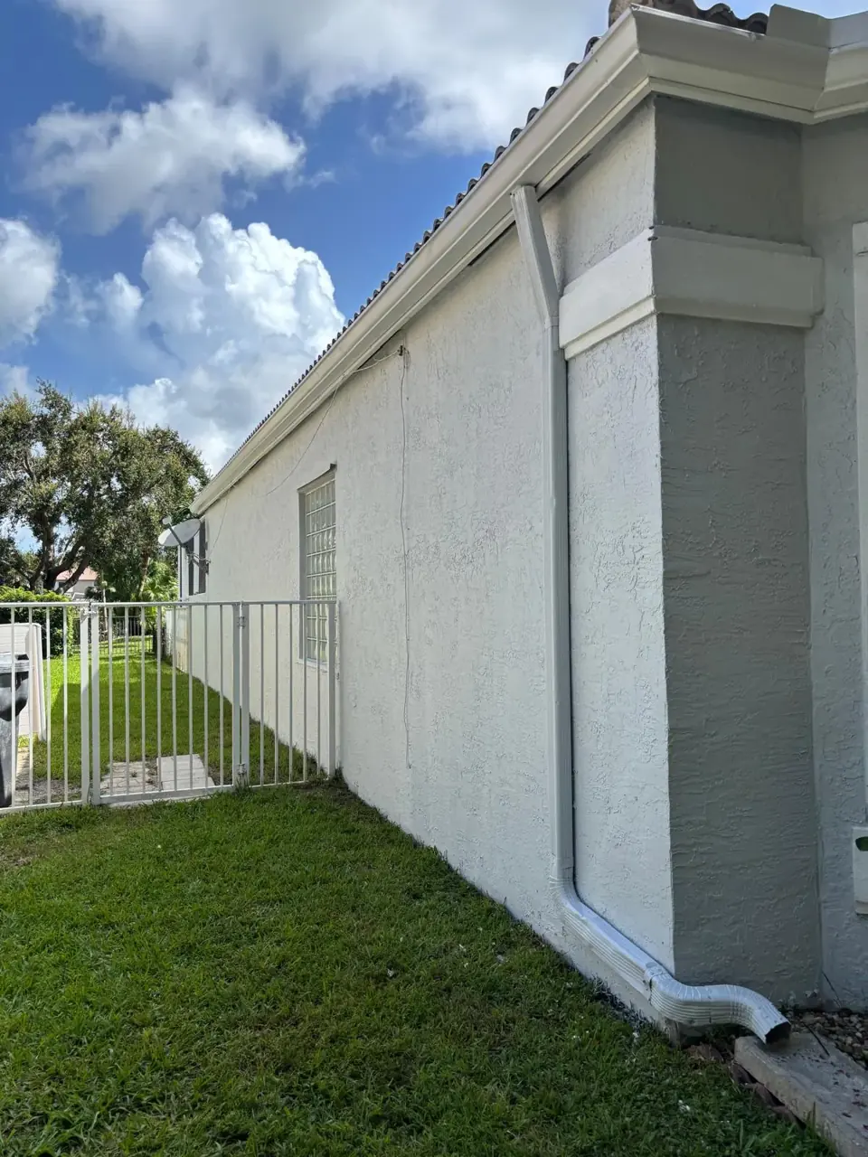 Downspout carrying water away from a freshly painted white stucco wall in South Florida, preventing efflorescence and staining