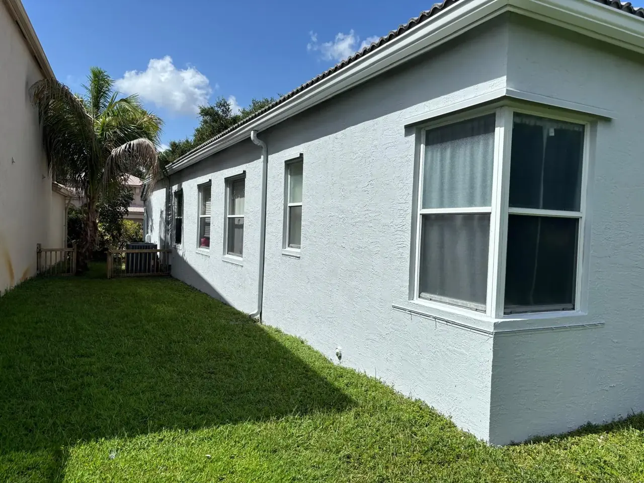 Freshly painted white stucco wall of a South Florida home with a bay window, green lawn and blue sky