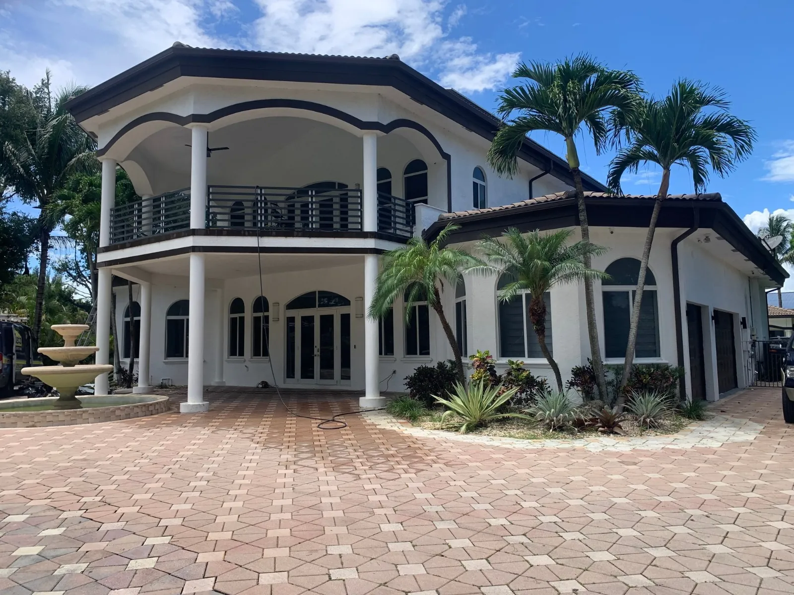 Two-story South Florida home repainted white with dark brown trim, a columned balcony, arched windows and palm trees in front