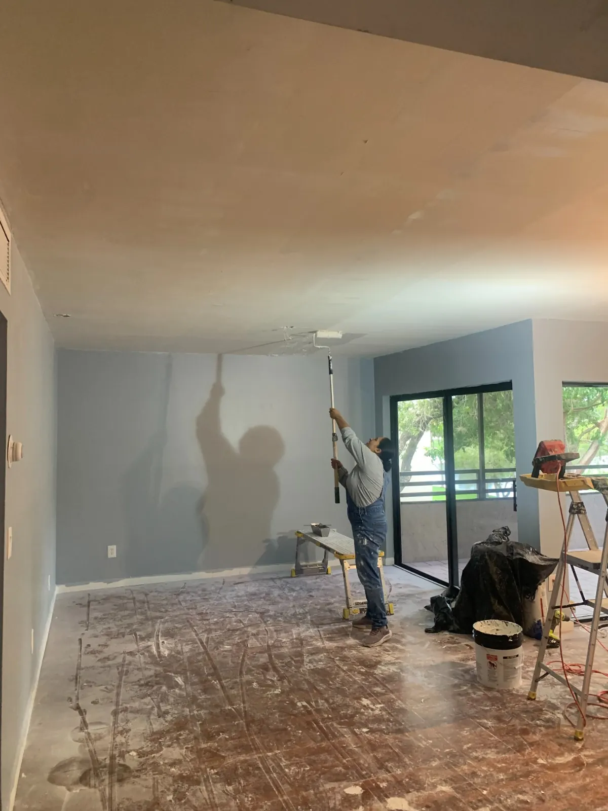 Painter rolling a finished condo ceiling with an extension pole