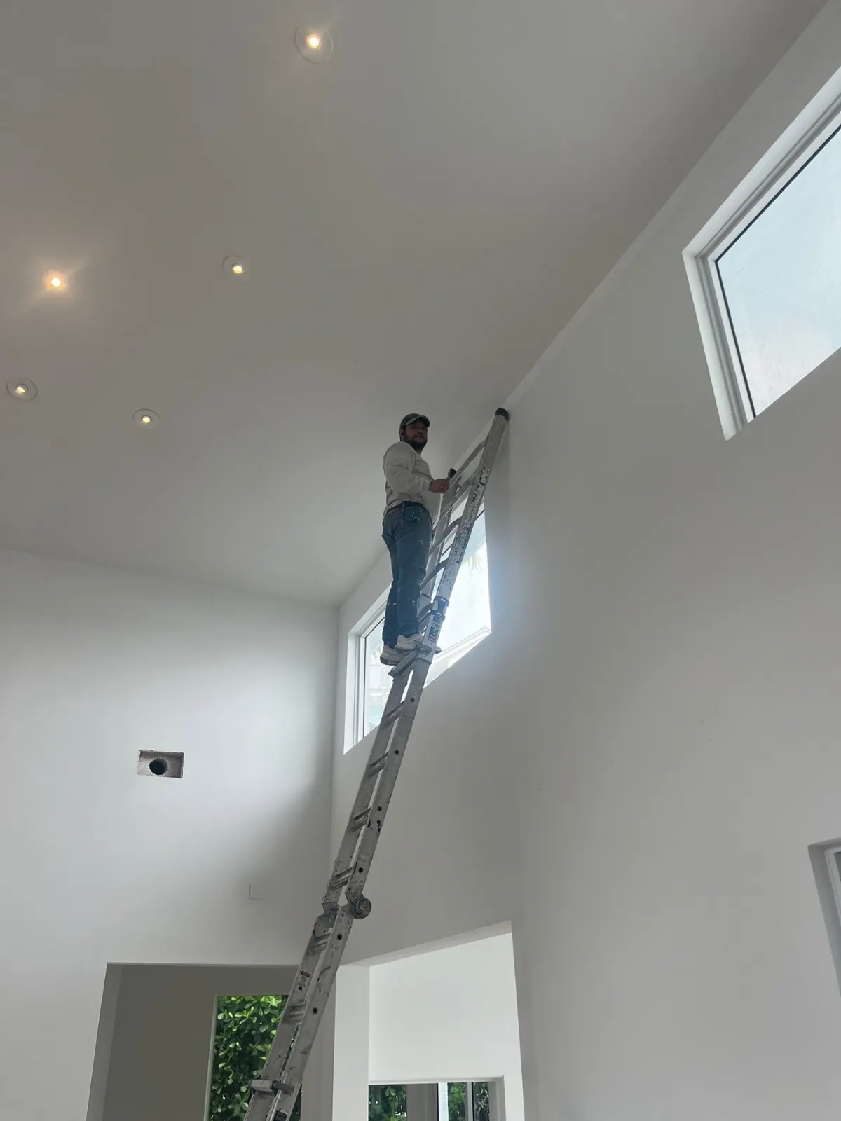 Painter on an extension ladder cutting in a two-story interior wall