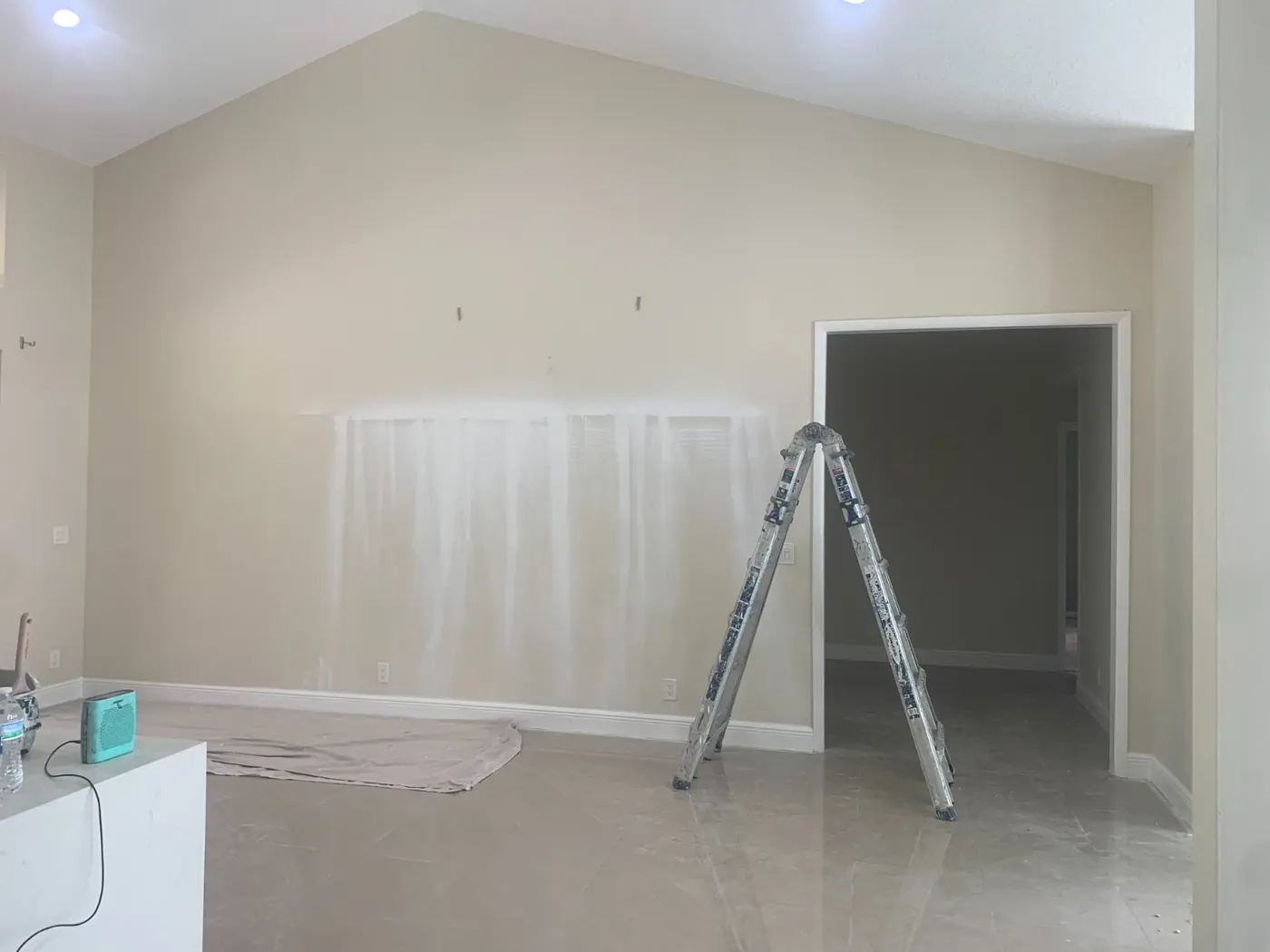 Wall being primed after skim coating, ladder and drop cloth in place
