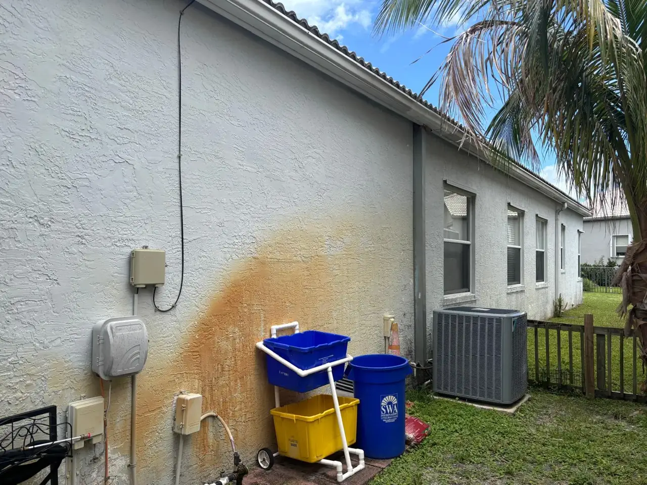 Orange iron stains fanned across white stucco on a South Florida house, caused by sprinkler water high in iron